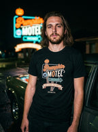 T-shirt noir Pumpkin Motel porté de nuit contre une voiture vintage, enseigne néon du motel en fond
